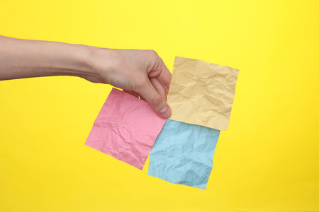 Woman's hand holds yellow crumpled memo piece of papers on yellow backgroundの写真素材