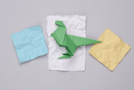 Origami dinosaur and crumpled pieces of paper on a gray background. children's creativity