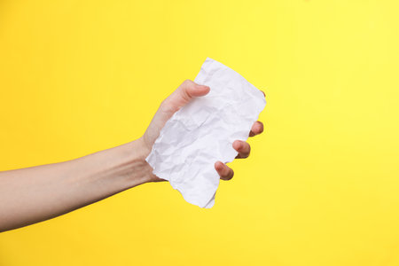 Woman's hand holds empty crumpled white sheet of paper on a yellow backgroundの写真素材