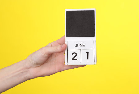 Woman's hand holds wooden calendar with date june 21 on a yellow backgroundの写真素材