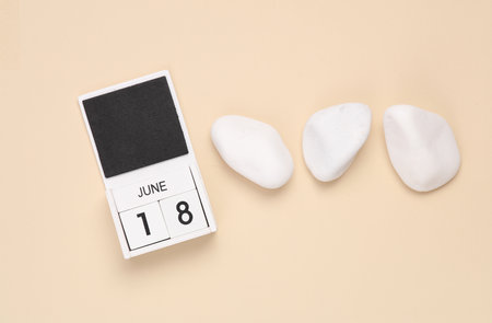 White wooden calendar with the date june 18 on beige background with white pebblesの写真素材
