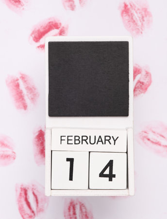 Lip print left by lipstick on white paper and White wooden calendar with the date february 14....