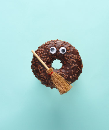 Chocolate donut with eyes and a witch's broom on a blue background. Halloween concept. Trick or Treatの写真素材