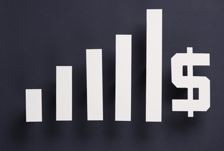 Paper-cut columns of a chart tending upwards and dollar symbol on a gray background. Analytics, business conceptの写真素材