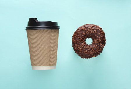 Cardboard cup of takeaway coffee with chocolate donut on blue backgroundの写真素材