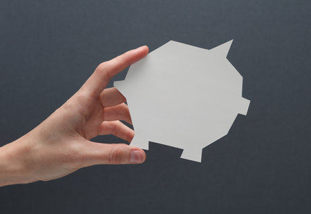 Hand holding a paper-cut piggy bank on a gray backgroundの写真素材
