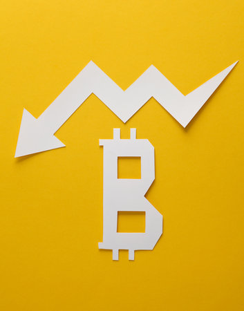 Paper cut bitcoin symbol with falling arrow on yellow backgroundの写真素材