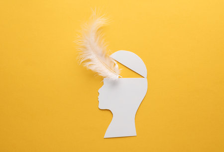 Paper-cut open human head with feather on yellow background. mental healthの写真素材