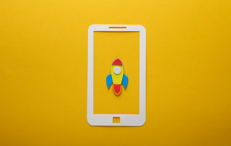 Paper-cut smartphone with rocket on yellow background. startup conceptの写真素材
