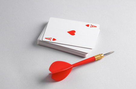 Ace of hearts on top of stack of playing cards and dart, gray backgroundの写真素材