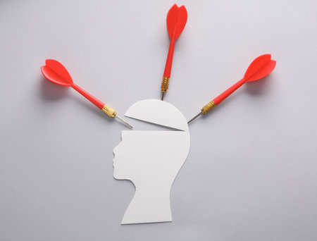 Paper-cut silhouette of a head with darts on a gray background. Headache conceptの写真素材