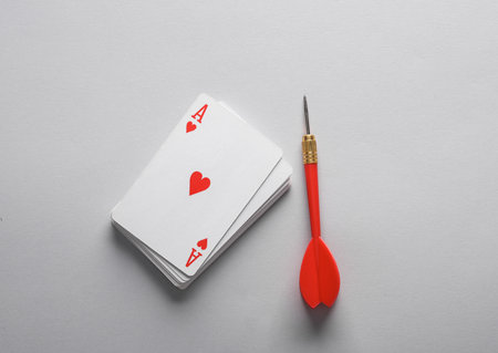 Ace of hearts on top of stack of playing cards and dart, gray backgroundの写真素材