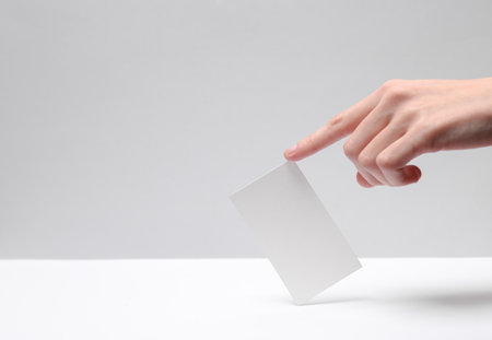 Female hand holding a business card with a finger on a white-gray backgroundの写真素材
