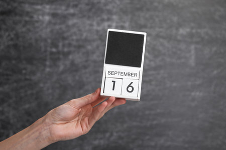 Wooden block calendar with date september 16 in female hand on background of school chalk blackboardの写真素材