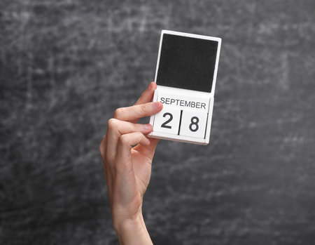 Wooden block calendar with date september 28 in female hand on background of school chalk blackboardの写真素材