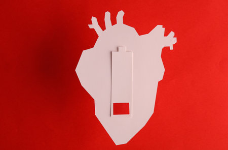 Paper-cut anatomical heart and a low battery on a red background. heart diseases