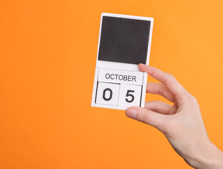 Wooden block calendar with date october 05 in female hand on orange backgroundの写真素材