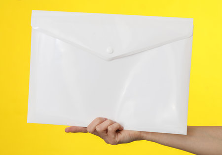 Female hand holding a white plastic folder on a yellow backgroundの写真素材
