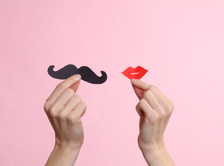 Hands holding lips and mustache on pink background. Carnival, photo booth, party conceptの写真素材