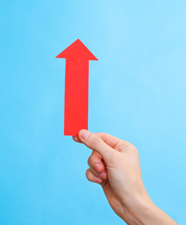 Red paper arrow in a female hand on a blue background. business conceptの写真素材