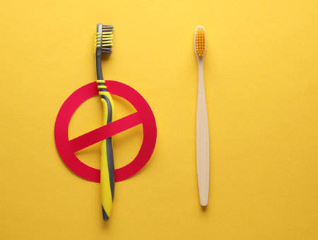 Plastic toothbrush with prohibition sign and bamboo toothbrush on yellow background. Plastic free, eco conceptの写真素材