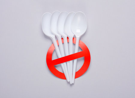 Plastic spoons with red prohibition sign on gray background. Plastic free, stop pollution, eco friendly concept. top view. flat layの写真素材