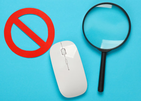 Pc mouse and magnifying glass with prohibition sign on blue backgroundの写真素材