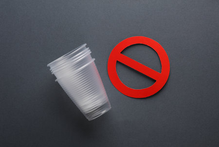 Plastic cups with red prohibition sign on dark background. Plastic free, stop pollution, eco...