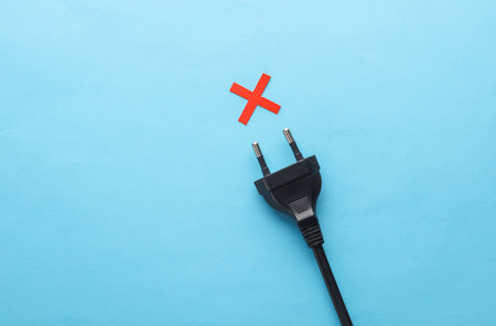 Electrical plug with red cross on blue background. Concept of electricity or energy saving.の写真素材
