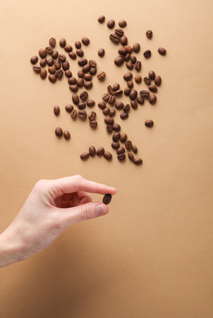 Hand holding roasted coffee bean on brown backgroundの写真素材