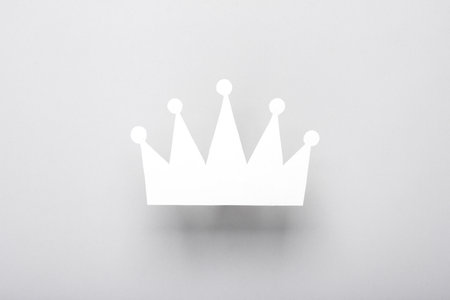 Paper-cut silhouette of a white crown on a gray background.