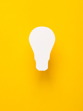 Paper-cut white silhouette of a light bulb on yellow background