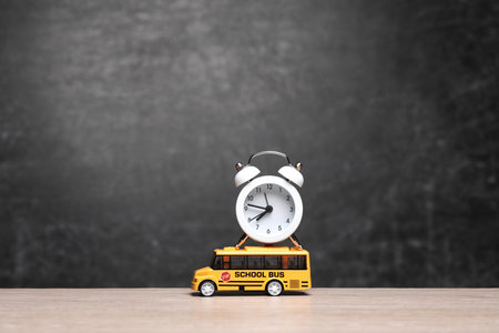 Miniature School bus with alarm clock on table against the background of chalkboard. back to school