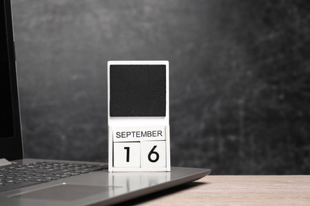 Calendar with september 16 date and laptop on table against chalk board backgroundの写真素材