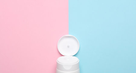 Open cream tube part on blue-pink background. top view