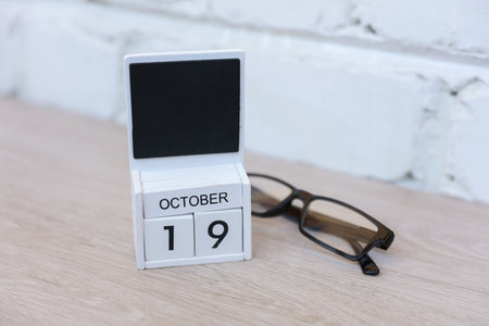 Wooden calendar with date October 19 and eyeglasses on table against brick wall background. Deadline, planning, business conceptの写真素材