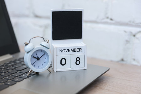 Wooden calendar with date November 08 and laptop with alarm clock on table against brick wall background. Deadline, planning, business conceptの写真素材