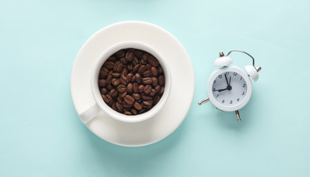 Ceramic coffee cup with coffee beans and alarm clock on blue background. top view