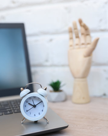 working space. Close-up of alarm clock with laptop and wooden hand. Business concept, deadline,...