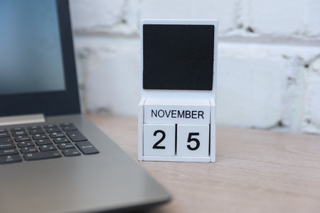 Wooden calendar with date November 25 and laptop on table against brick wall background. Deadline, planning, business conceptの写真素材