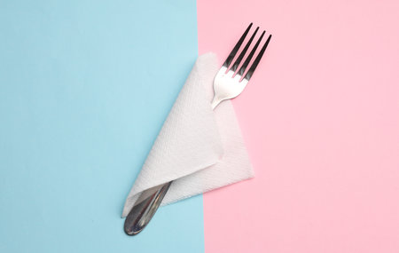 Metal fork with napkin on blue-pink background. top view