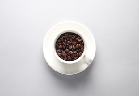 Ceramic coffee cup with coffee beans on gray background. top viewの写真素材