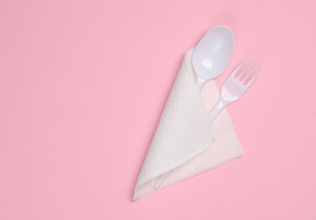 Plastic fork with a spoon and a napkin on a pink background. Picnic, top viewの写真素材