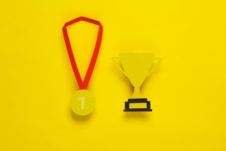 Paper-cut gold medal and winner cup on yellow background. First place. Competition, prize, trophies, winners award. flat lay. top viewの写真素材