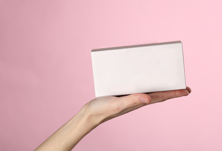 Empty white cardboard box on the palm of a female hand on a pink backgroundの写真素材