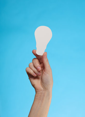 Hand holding paper-cut light bulb on blue backgroundの写真素材