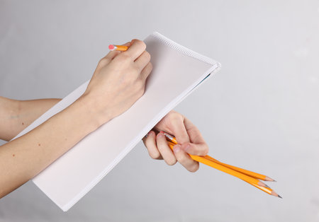 Female hands draws with pencil in empty white sketchbook on gray backgroundの写真素材