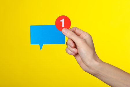 Hand holding Paper cut yellow Notification speech bubble with 1 number on pink background. Social media chat, message, sms, subscribe notice alert and reminder.の写真素材