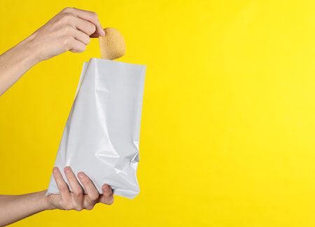 Female hand holding mock up pack of chips on yellow background. Template for designの写真素材
