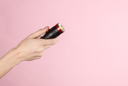 Female hand holding a flashlight on a pink background